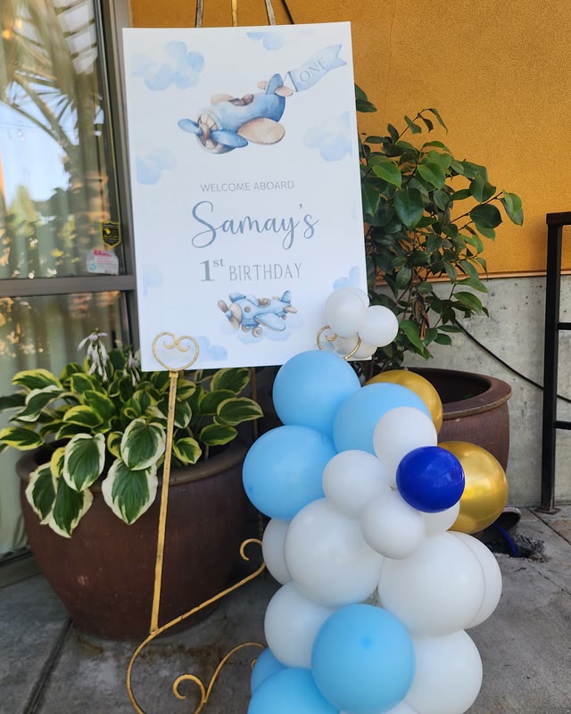 Aeroplane-themed first birthday welcome sign with a blue and white balloon column