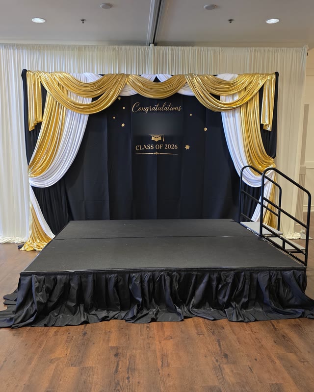 Black and gold graduation stage with a draped backdrop and celebration sign