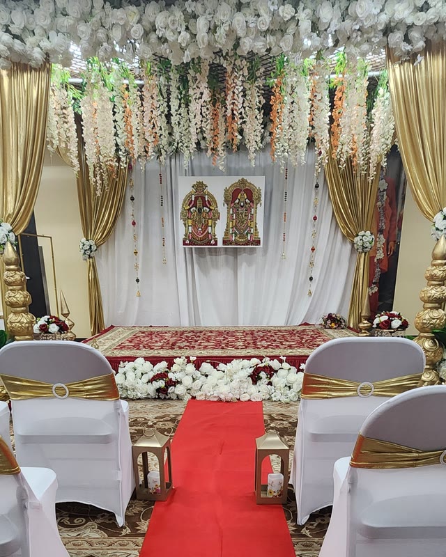 White and gold draped backdrop with deities, a red aisle and covered chairs