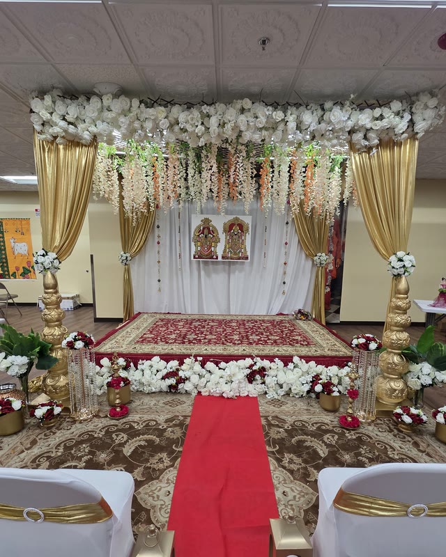 Gold-draped ceremony stage with a floral canopy, patterned rug and red aisle