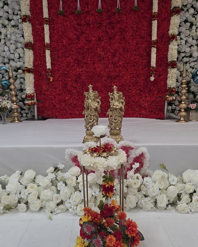 Deep red floral backdrop with brass idols and fresh white flower arrangements