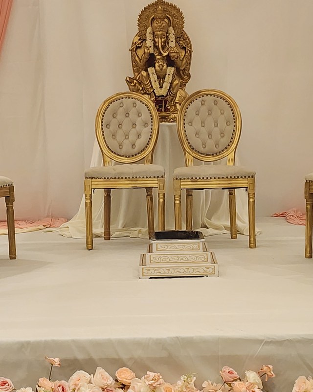 Cream draped dais with gold chairs and a blush rose garland along the stage edge