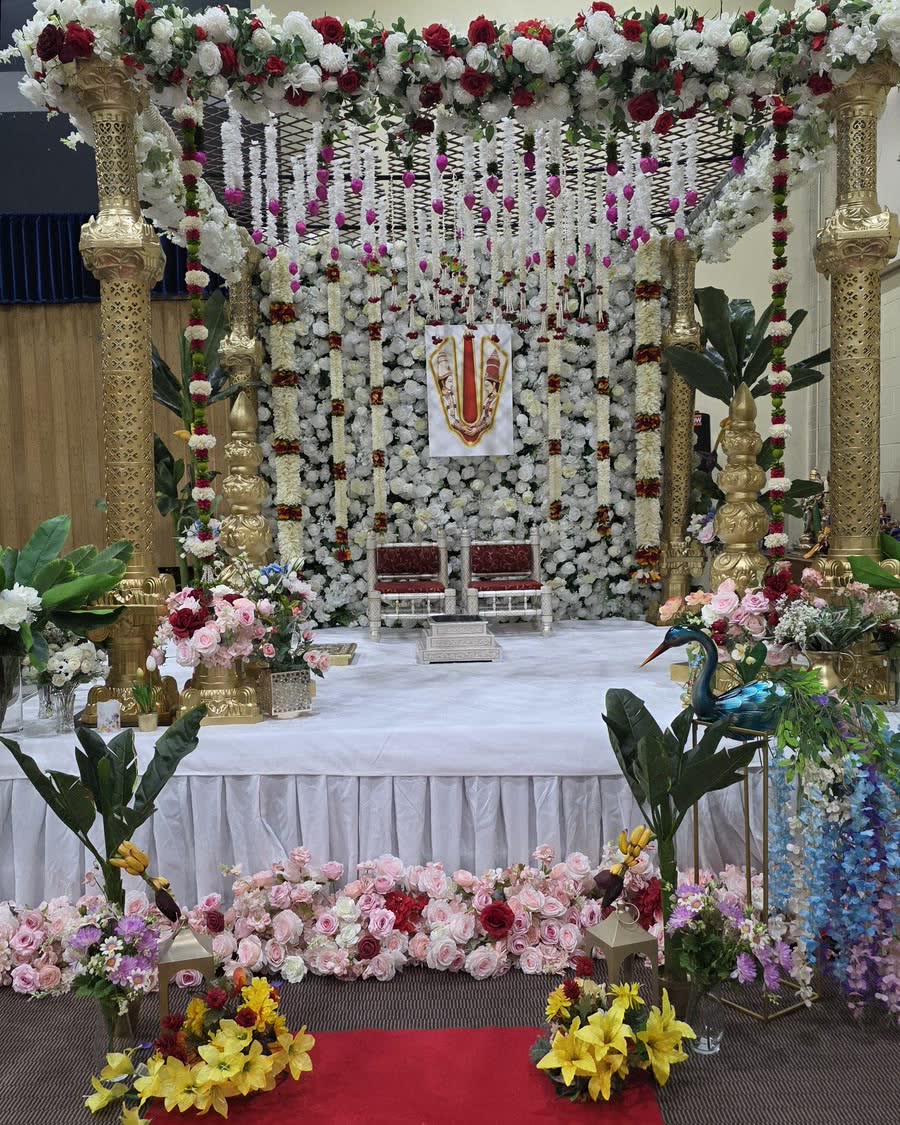 A Nani Event Decors ceremony mandap with gold pillars, hanging florals and a red carpet aisle